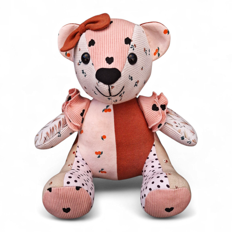 Roze speelgoedbeer met hartjes en een strikje, gemaakt van verschillende stoffen.